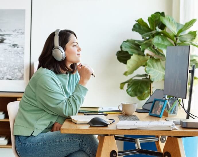 Mulher com auscultadores, a segurar uma caneta e a olhar para um monitor de PC