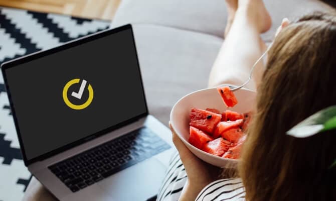 Mulher a comer fruta ao lado de um computador portátil aberto